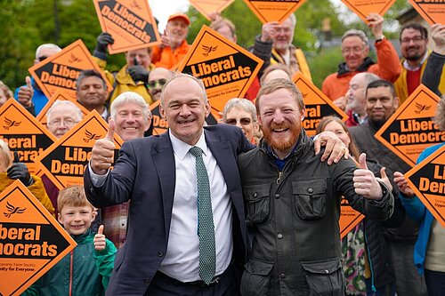 Ed Davey with members of Newcastle Lib Dems holding up Liberal Democrat orange diamond placards