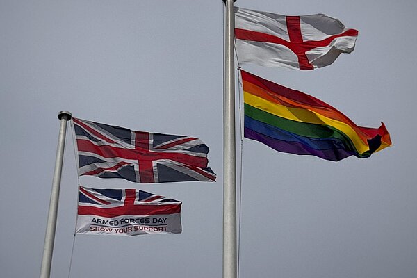 Two flagpoles each with two flags on, one flying the Union and Armed Forces Day flags, the other flying St George's flag and the Pride flag