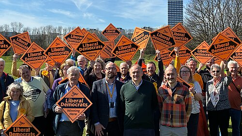Ed Davey with members of Newcastle Lib Dems holding up Liberal Democrat orange diamond placards