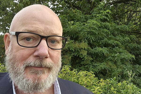 Stephen Kelly in front of trees and bushes