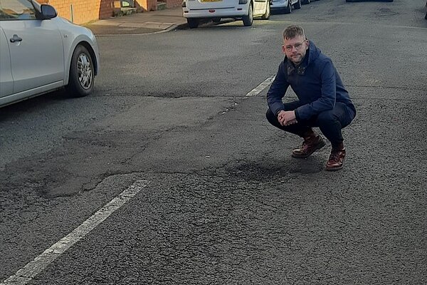 Andrew crouching over the broken road surface on Cartington