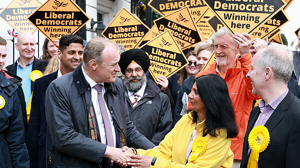 Ed Davey greeting woman in front of crowd with Lib Dem diamond signs